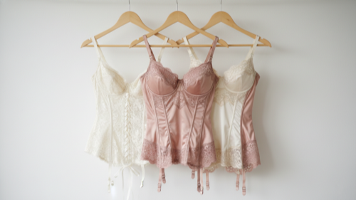 Structured Lingerie Styles Hanging corset, bustier, and basque on white wall. Ivory and rose tones.